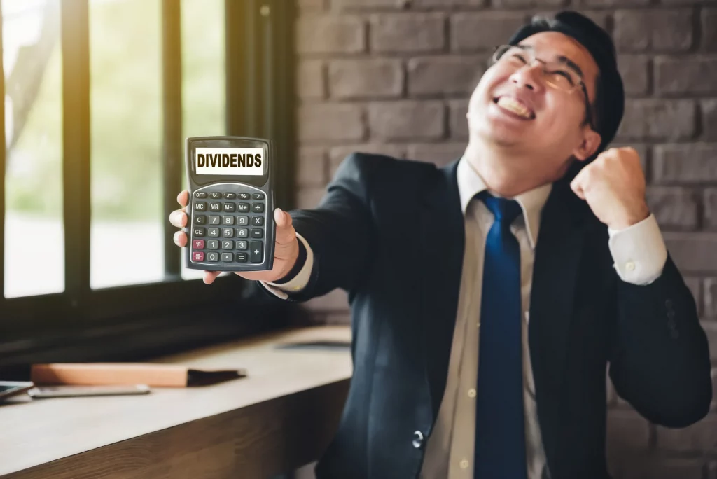 An image for our startup newsletter. The image depicts a person holding a calculator that says "Dividends" on it, a symbol for investment.